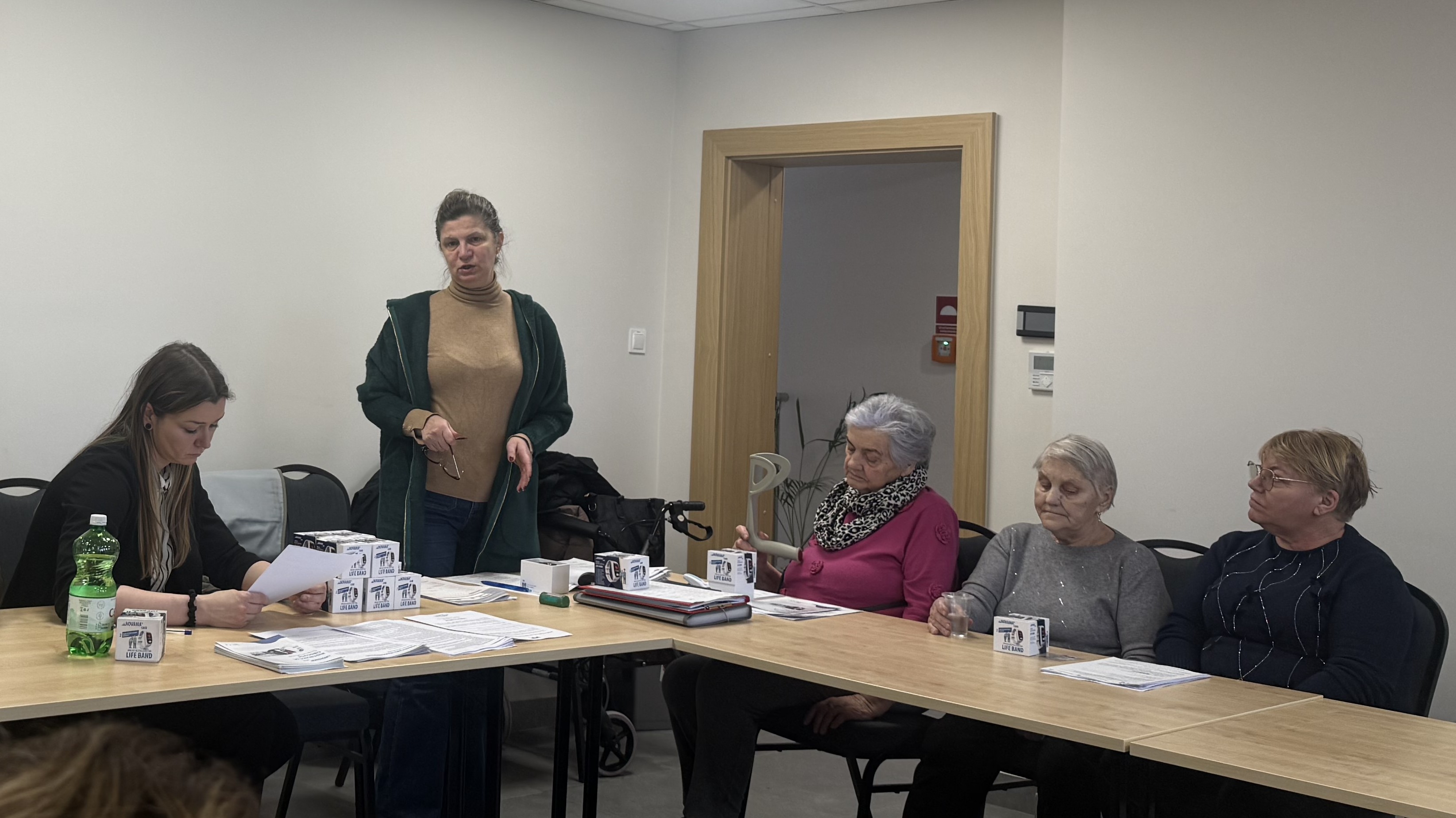 Prowadząca tłumaczy ludziom siędzącym przy stole cele programu